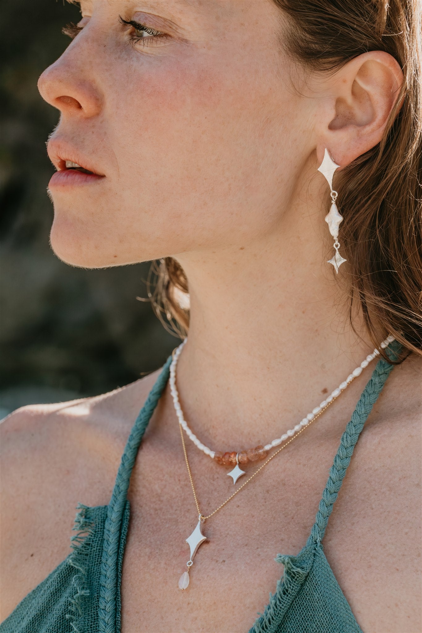 Woman wearing star-shaped earrings and necklaces with a blurred natural background