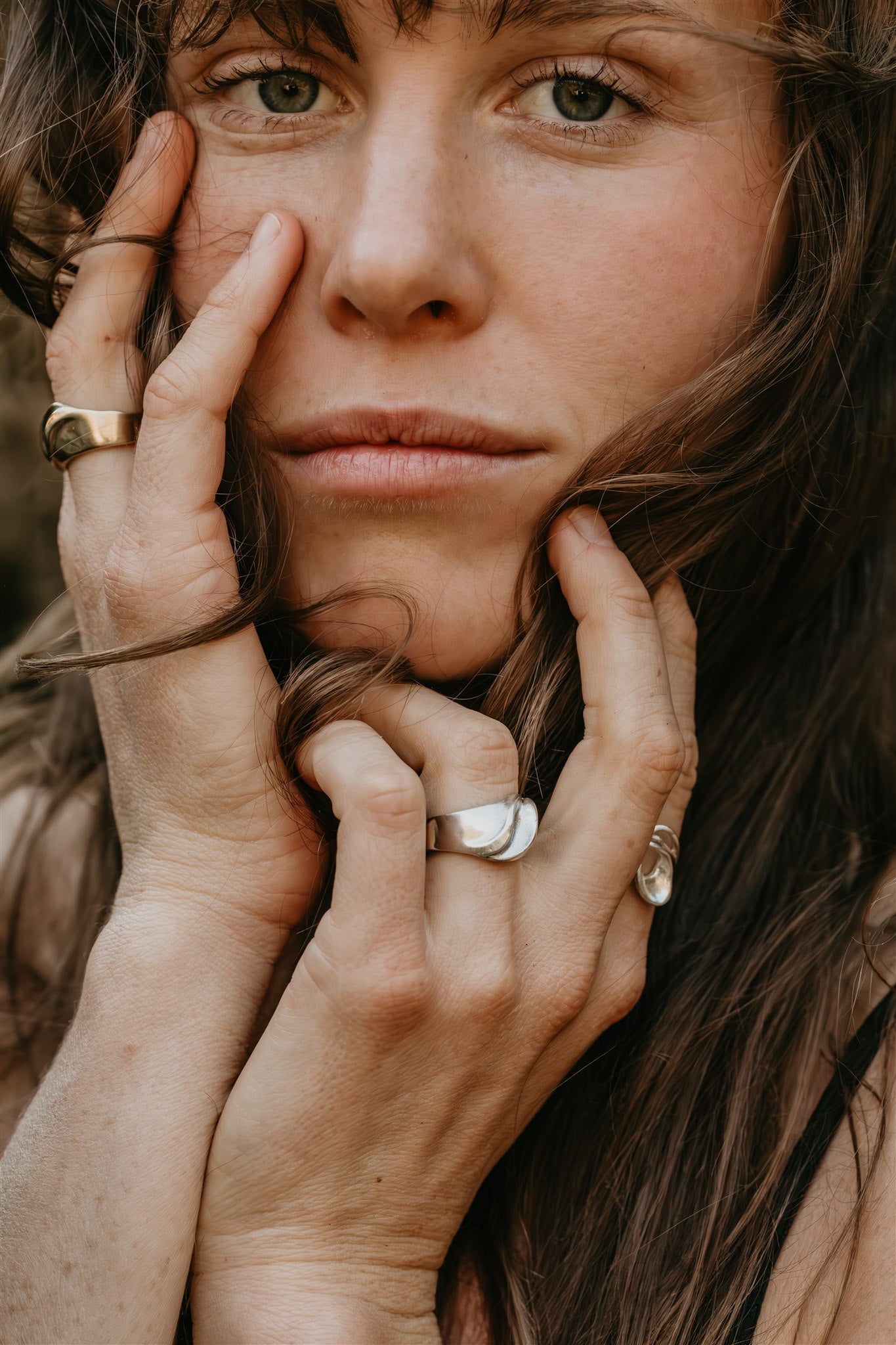 Close-up of a woman with her hands near her face, wearing rings.