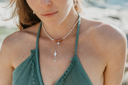 Close-up of a person wearing multiple necklaces with a blurred natural background