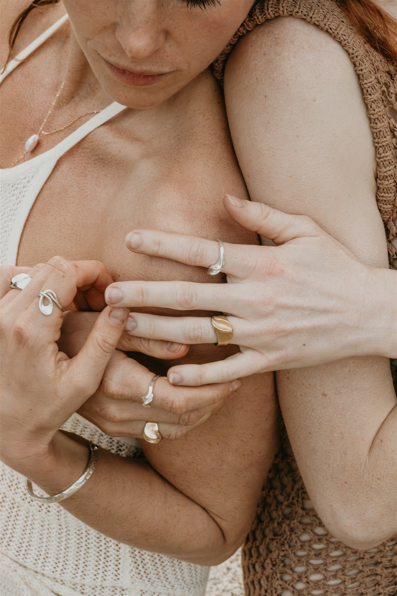 Close-up of two people holding hands with visible jewelry against a neutral background