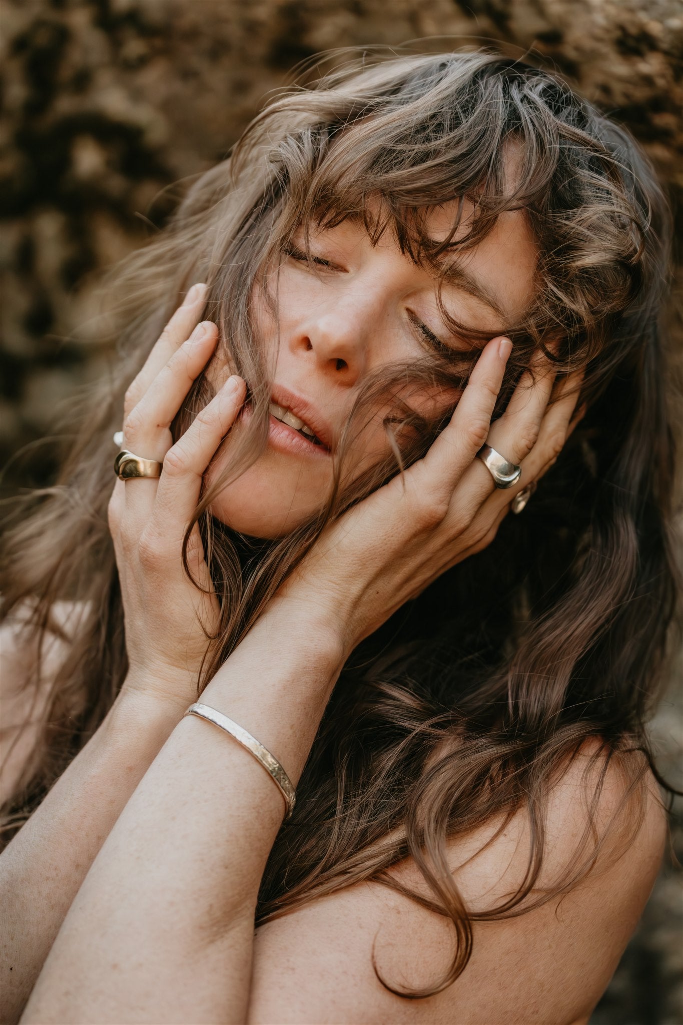 Woman with long hair and rings on her fingers against a blurred natural background