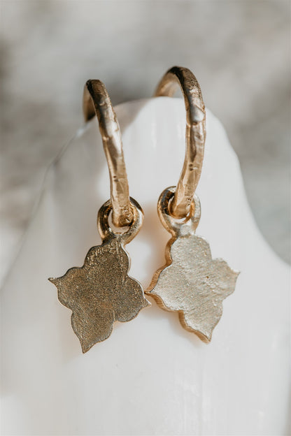 Gold hoop earrings with leaf-shaped charms on a white shell.