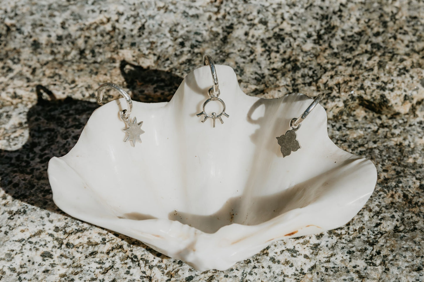 Silver earrings displayed on a white shell against a textured stone background