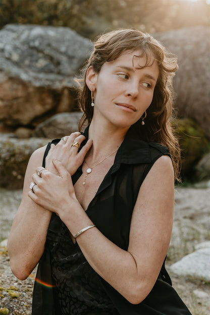 Woman in a black dress standing outdoors with rocks and natural light in the background