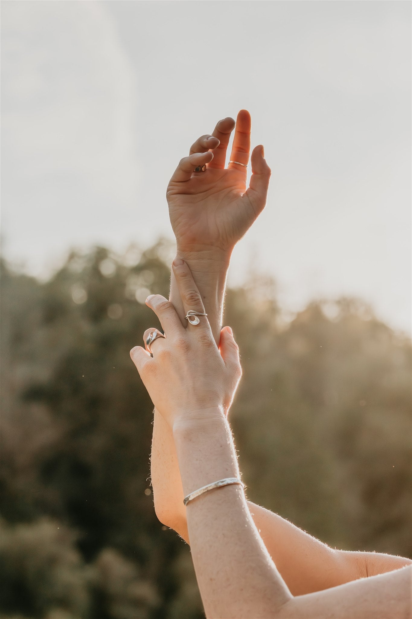 Two hands reaching towards each other with blurred natural background, wearing jewelry