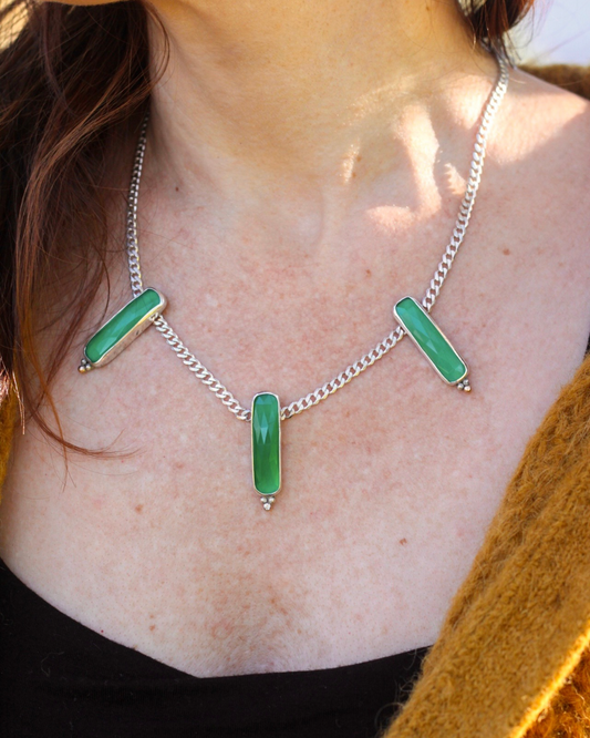 Necklace with green pendant on a person wearing a mustard-colored garment.