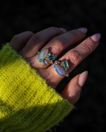 Hand wearing multiple rings with gemstones against a dark background