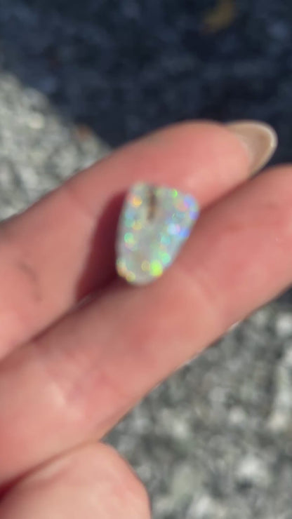 a video close-up of a opal stone with several different colors, held in a hand with a rocky background.