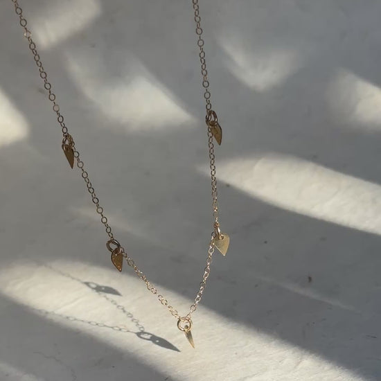 a video of a gold dainty necklace with 5 small charms against a white background
